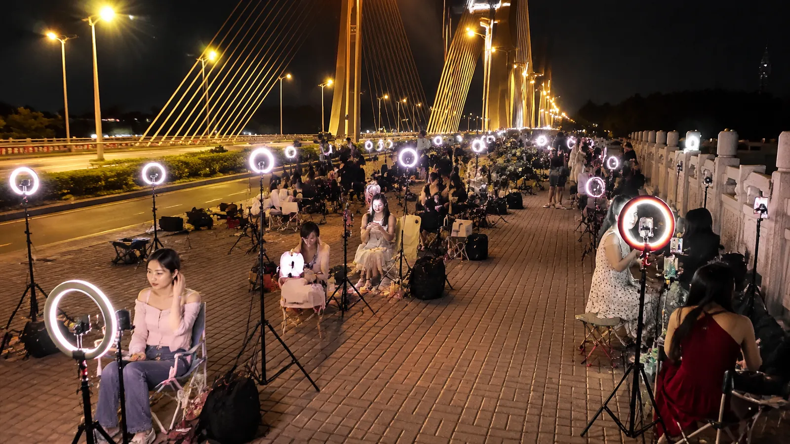 Chinese street livestreamers sitting beside a row of glowing ring lights at night