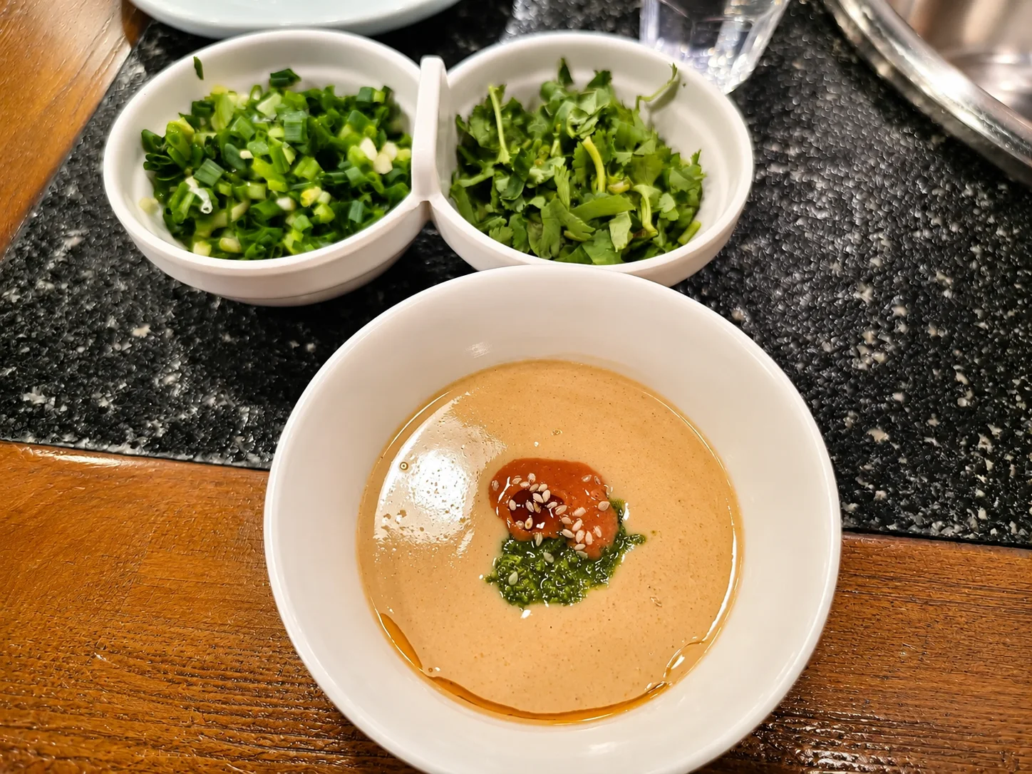 A small bowl of thick sesame sauce with chopped scallions and cilantro, served as the classic dipping sauce for Beijing copper-pot mutton