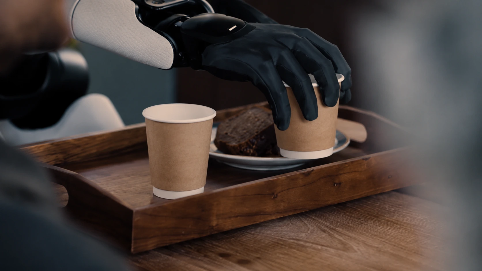 A human trainer guides a humanoid robot as it reaches toward an ordinary paper cup in a real-world training space
