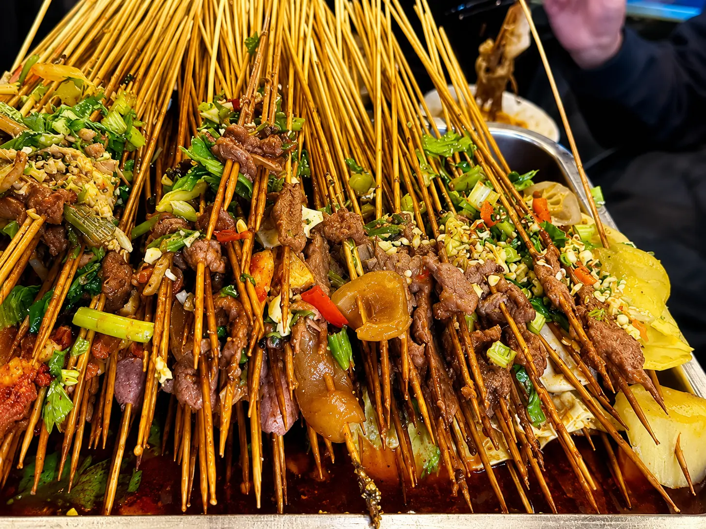 Dozens of small bamboo skewers threaded with meats and vegetables arranged on a tray