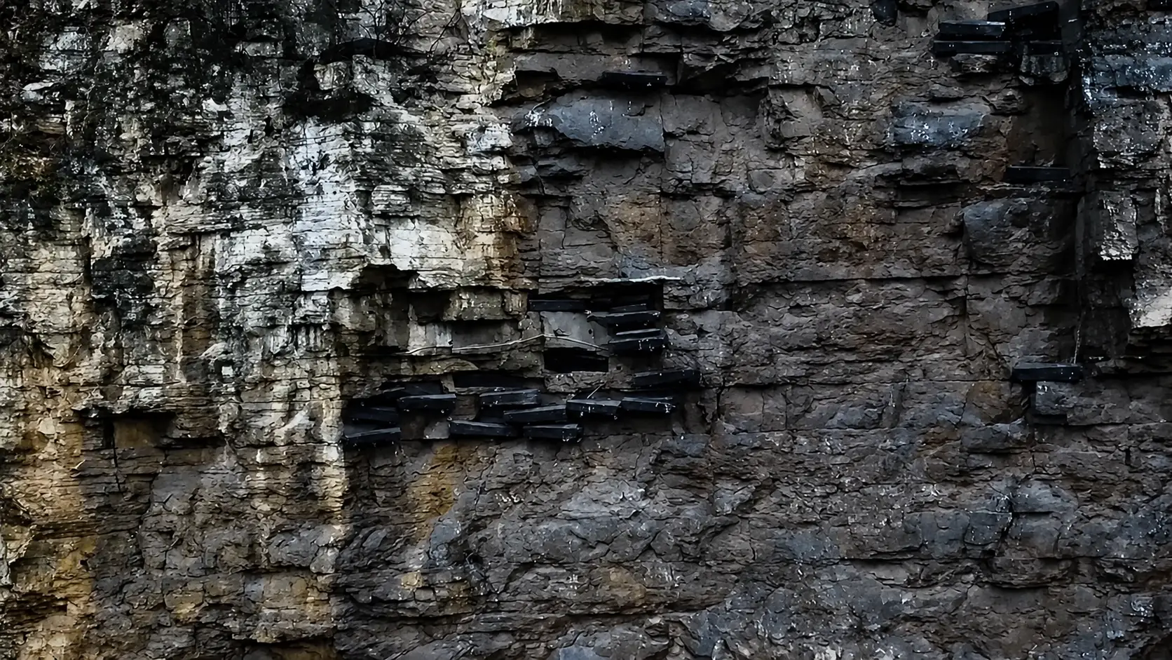 Side view of coffins on smooth rock with no walkway