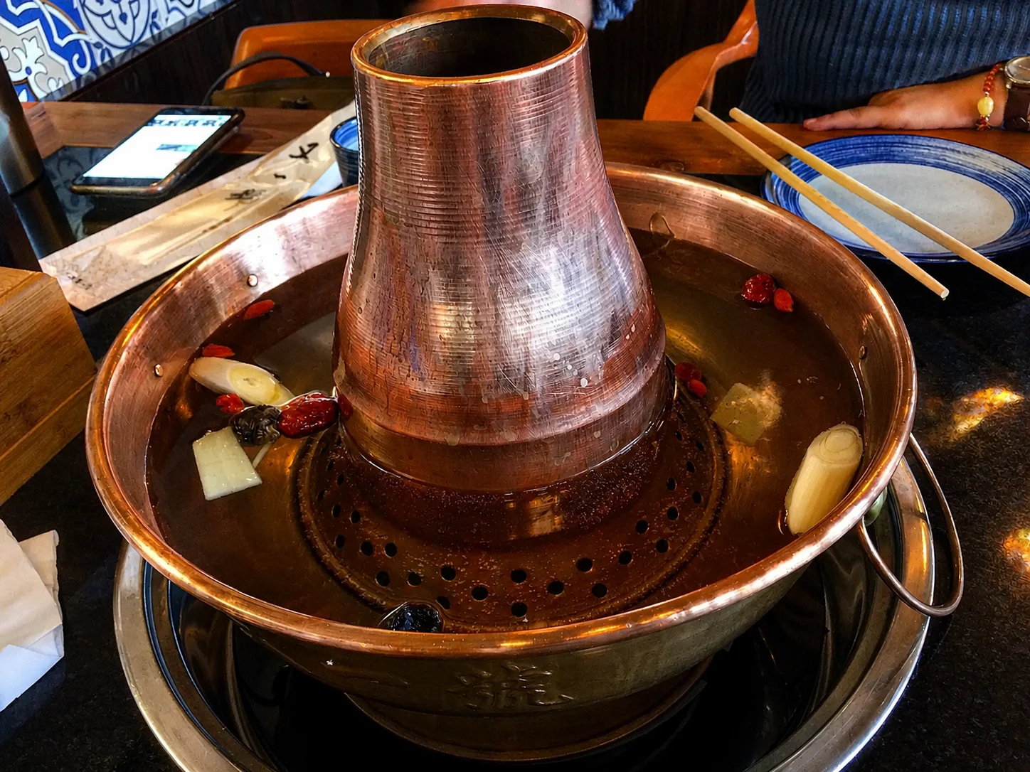 A traditional copper hot pot with clear boiling broth and a few goji berries floating on top