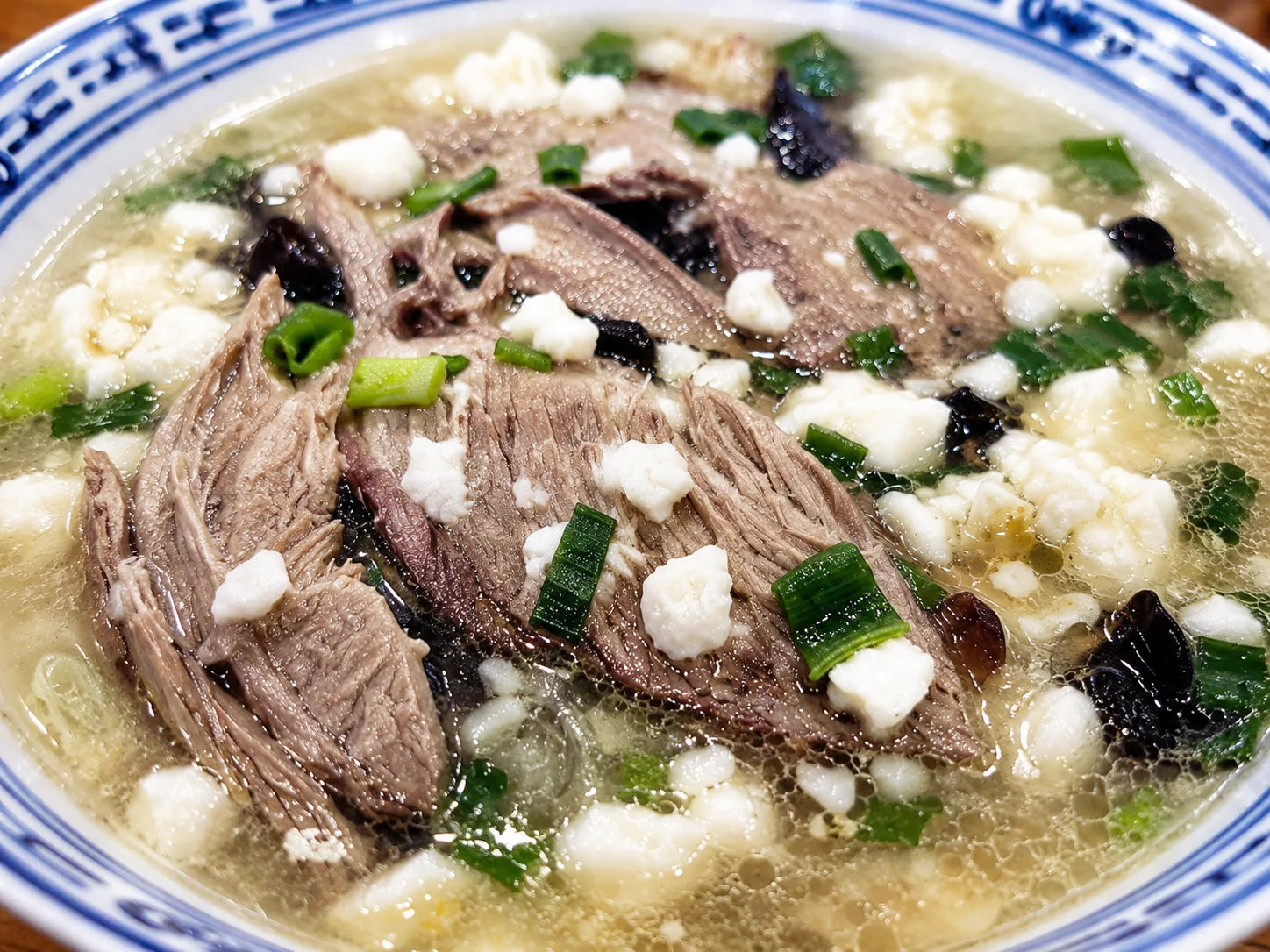 A finished bowl of yangrou paomo topped with lamb, cilantro, and chili oil
