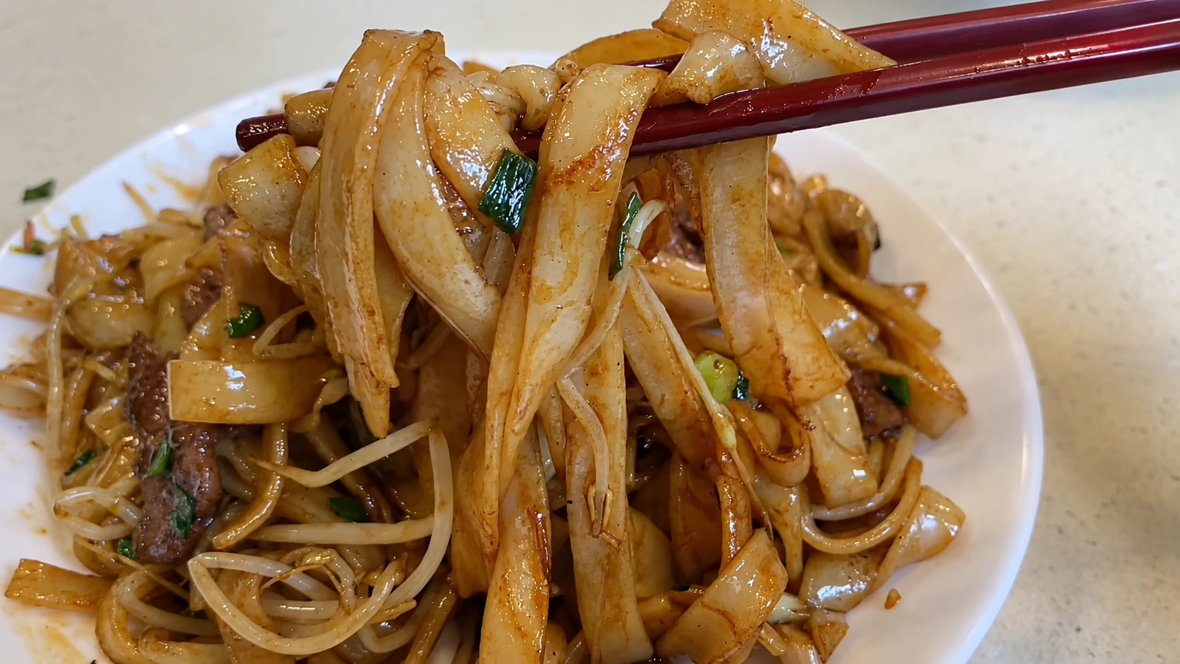 A plate of beef chow fun with wide rice noodles, tender beef slices, bean sprouts, and scallions in a glossy soy-based sauce