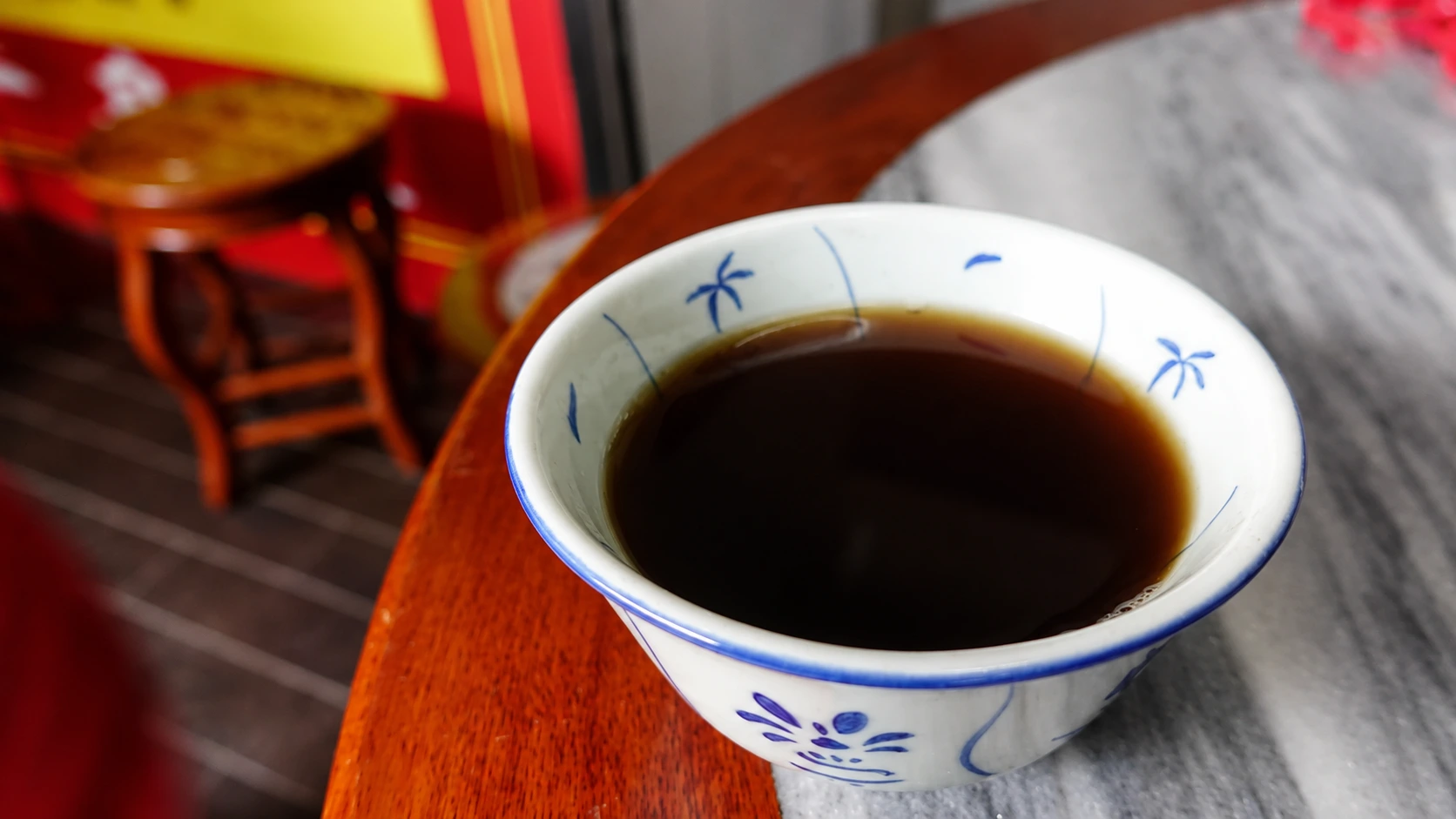 A ceramic bowl of dark herbal tea sits on a worn wooden counter in a Guangzhou liang cha shop, a copper pot steaming behind it