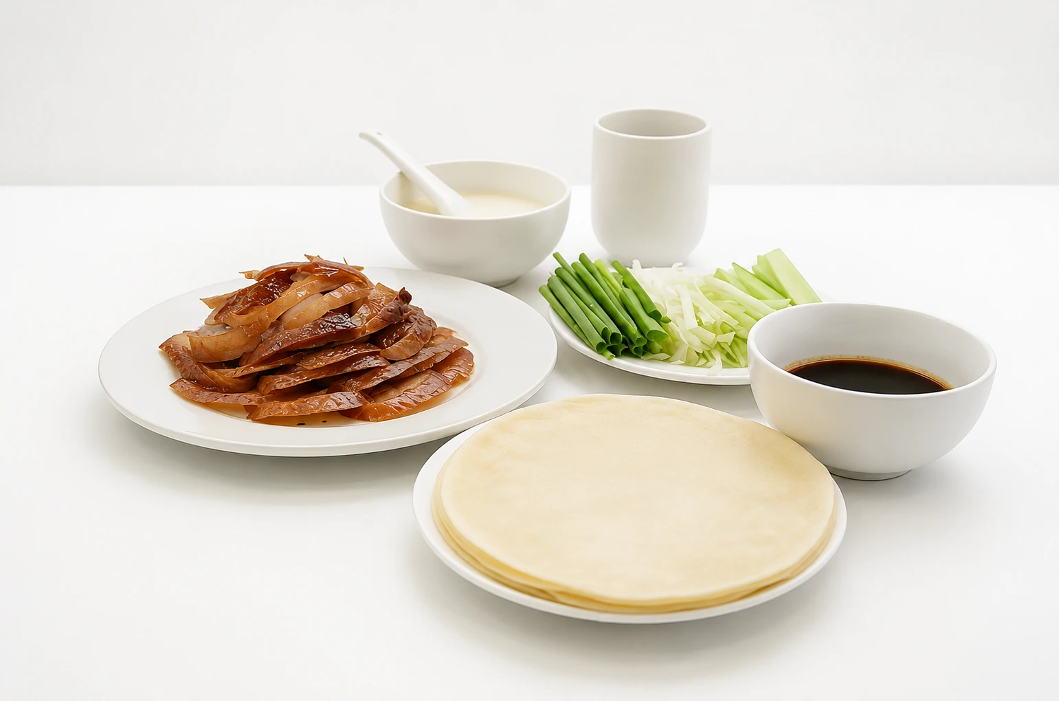 Sliced roast duck arranged on a plate beside thin spring pancakes, scallion strips, and dark sweet bean sauce