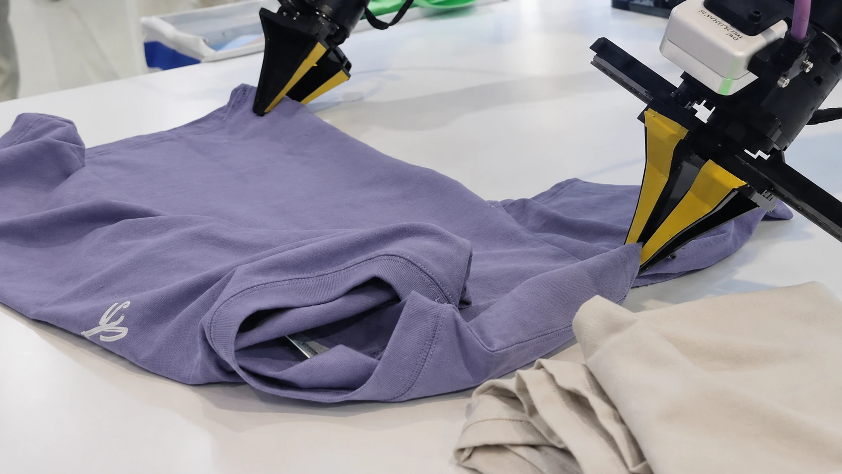 A robot arm struggles to fold a crumpled T-shirt on a table