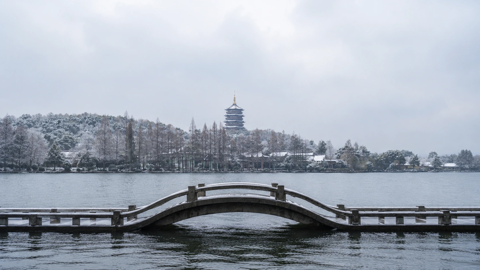 A quiet West Lake in Hangzhou under fresh snow with misty hills behind