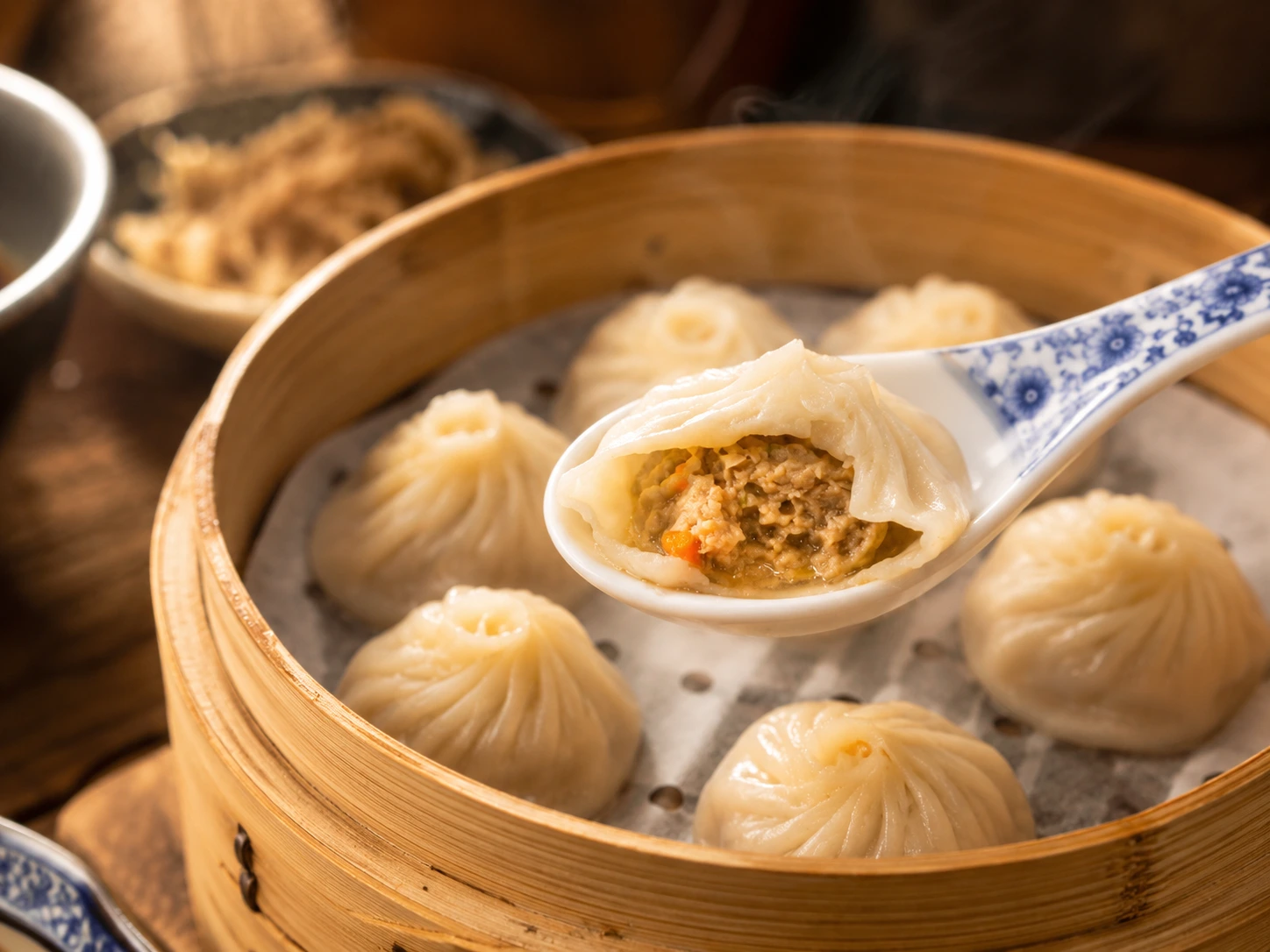 A xiaolongbao on a spoon with hot soup spilling from its wrapper