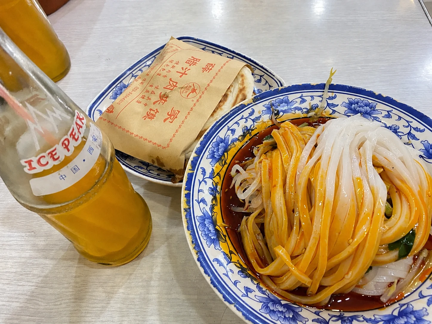 A Xi'an lunch table with roujiamo, liangpi, and a glass bottle of orange soda