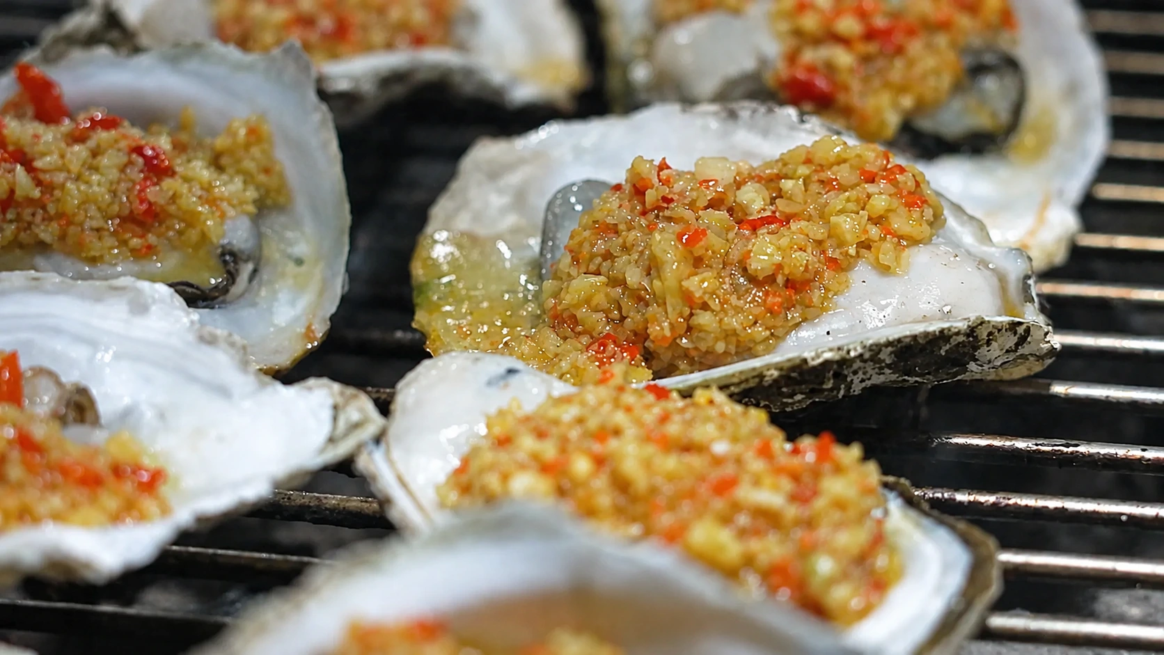 Charcoal-grilled Guandu oysters bubbling in their shells on a metal rack at a Zhanjiang night market