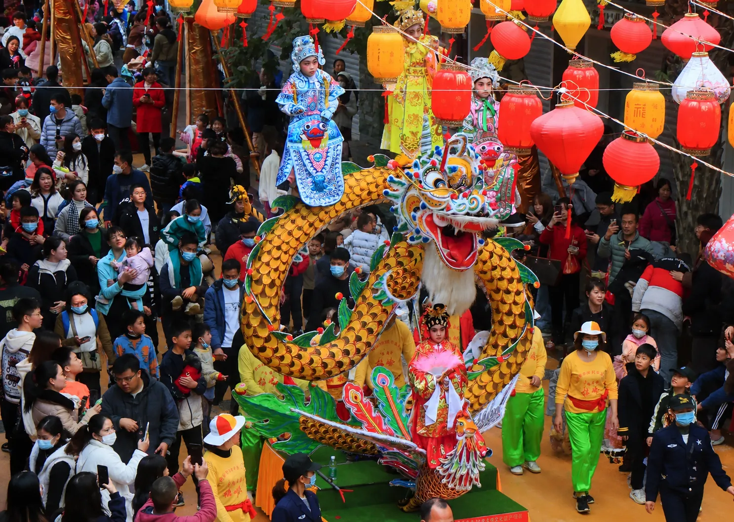 A decorated parade float carries costumed performers through a festival street