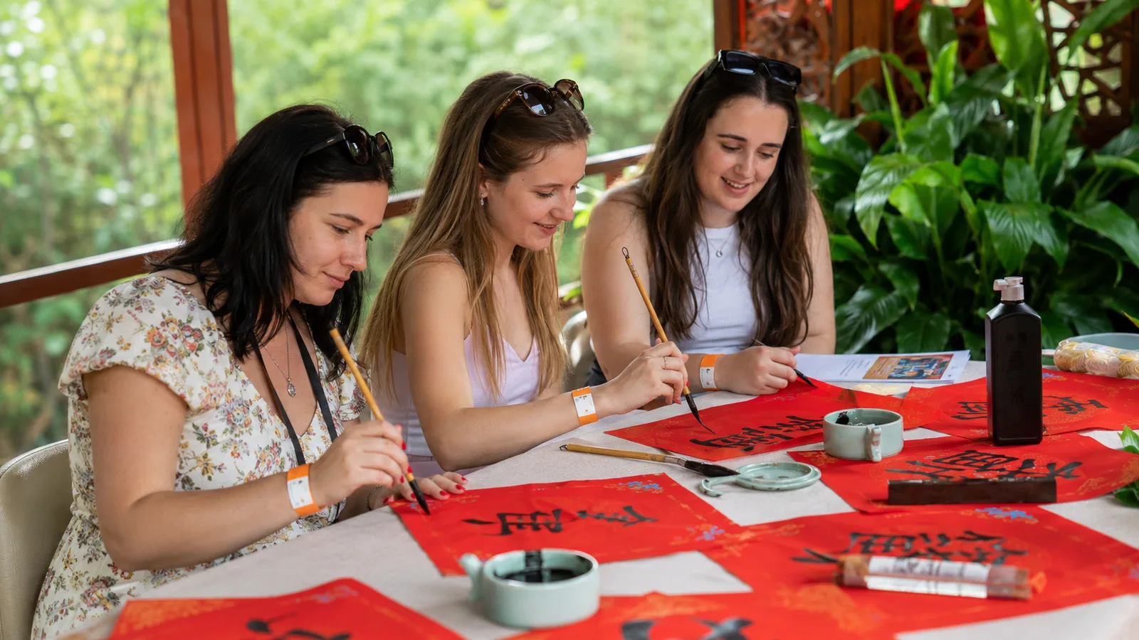 Three visitors practicing Chinese calligraphy at a table